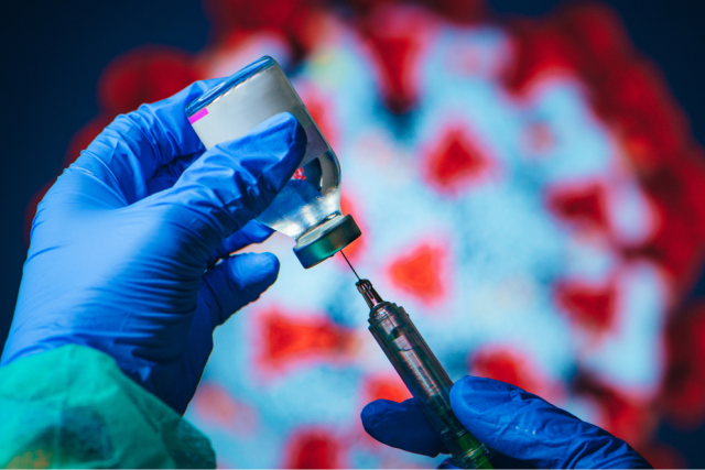 Gloved hands drawing a COVID-19 vaccine dose from a vial with a syringe, with a virus illustration in the background.
