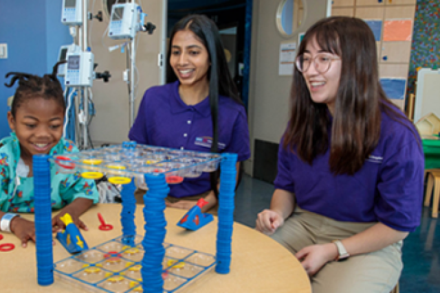 Text reads “Serve your community…medical field!” with “APPLY NOW” in yellow box, beside a child playing with red rings.