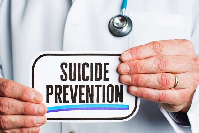 Anonymous doctor in lab coat holding suicide prevention sign