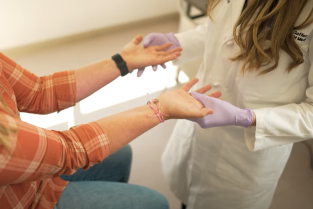 A doctor gently holding a patient's hand as she inspects them during surgical or medical consultation.