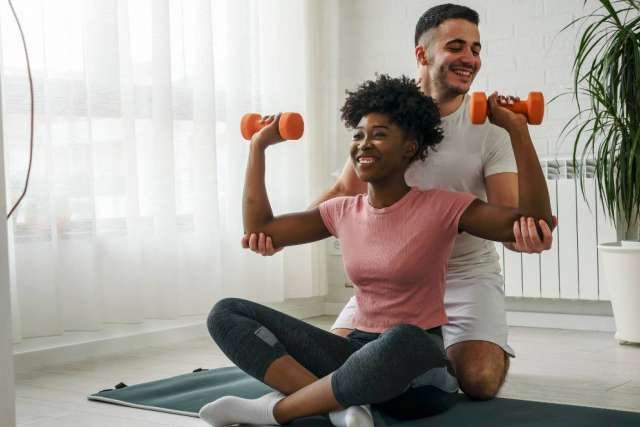 Man assisting girl doing seated dumbbell presses