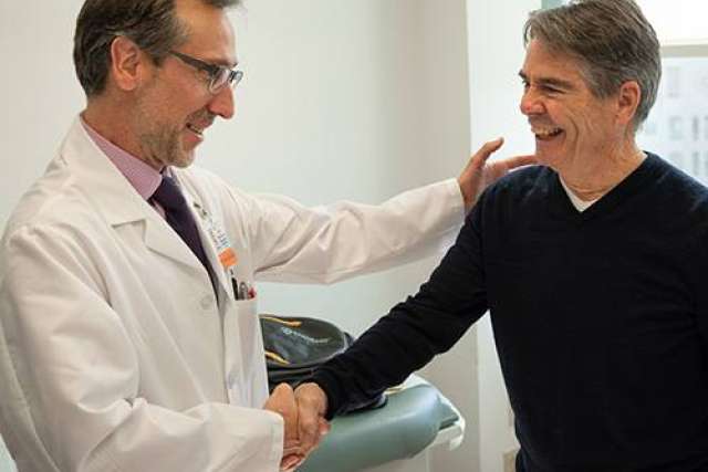 Healthcare professional in a white coat shaking hands with another person in a clinical setting.