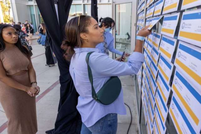Eden Patton watches as Justine Seivright finds her Match Day envelope on a wall of white, yellow, and blue envelopes.