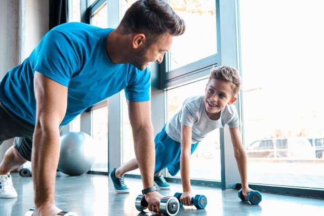 Father and son workout, man and boy doing push-ups facing each other in a gym.