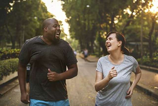 Obese couple working out, jogging side by side and smiling on a tree-lined park path