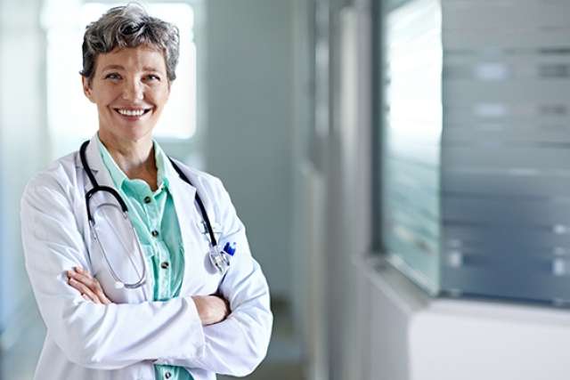 A physician standing with arms crossed, with a smile in greeting
