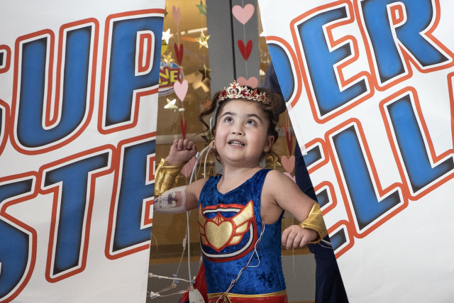 Pediatric patient Stella Rodriguez crashes through the banner at her superhero-reveal party.
