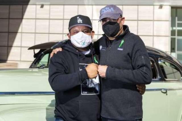 Louie Mejia fist bumping Dr. Anjay Rastogi in front of a green classic car