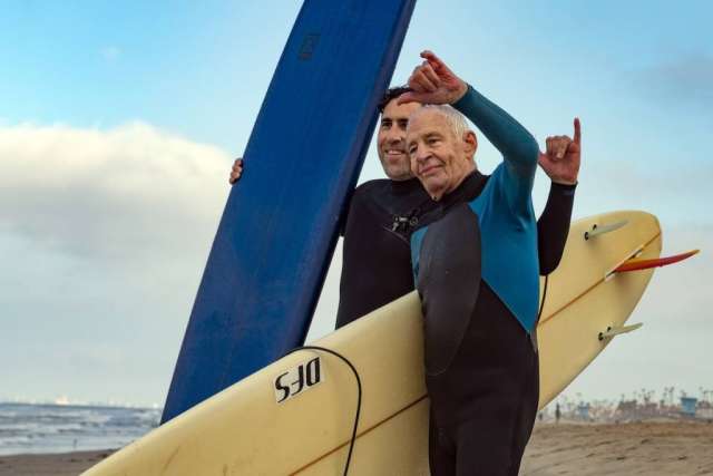 Dr. Sassoon and Robert Lombard  throwing up a "hang loose" sign with their hands on the beach