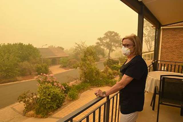 Woman stands on porch looking out at smoke from fire