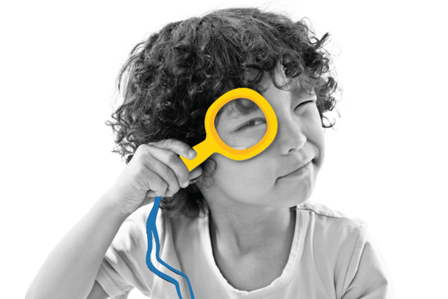 A black and white portrait of a child with curly hair, holding a yellow magnifying glass to their eye. The magnifying glass and its blue lanyard are in color.