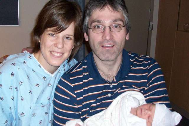 Smiling parents holding a swaddled newborn baby