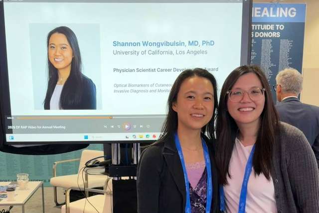 Two smiling women standing at a conference booth with a display behind them