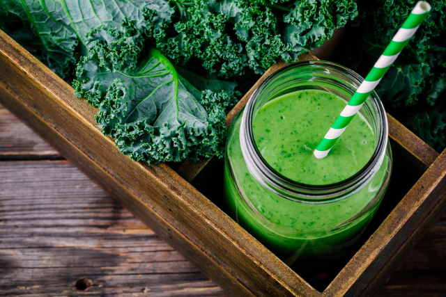 Green kale smoothie in jar with striped straw beside fresh kale leaves