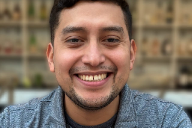 Smiling young man facing camera with blurred outdoor background.