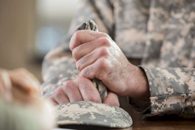 Caucasian male veteran squeezes camouflage uniform hat during counseling session. Close up is of the man holding the hat.