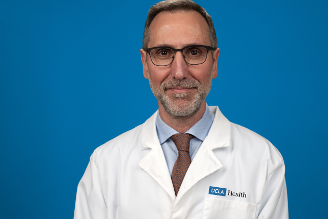 Dr. Antoni Ribas standing in front of a blue backdrop wearing his lab coat.