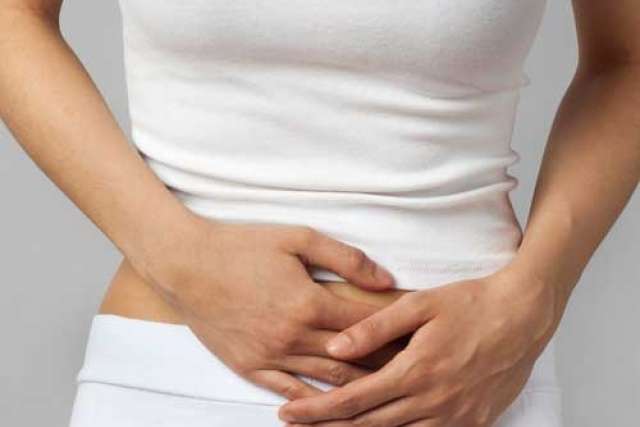 Woman in a white top holding her stomach, showing signs of discomfort.