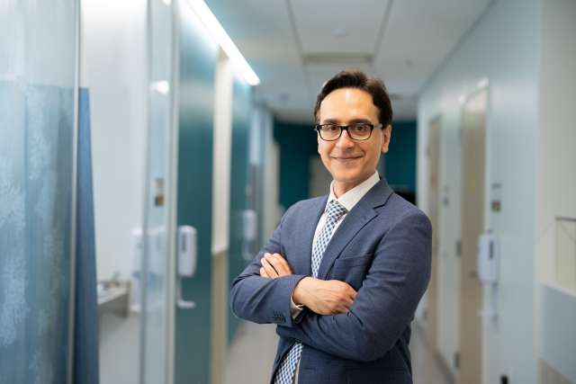 Dr. Amir Iravani in suit with arms crossed in office hallway.