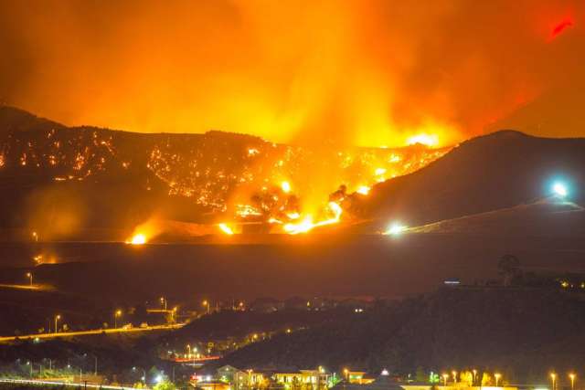 Hillside fires burning at night above illuminated town
