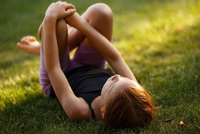 Child lying on grass, holding knees, enjoying a sunny day.