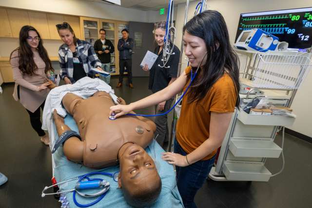 Rita Manukyan, left, Hilary Koenig and a Rosenfeld Hall guest get a close look at the computerized patient simulator in the form of a lifelike manikin.