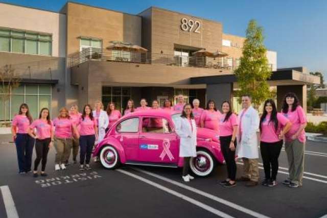 The team at UCLA Health San Luis Obispo Cancer Care gather around the hot pink VW Beetle