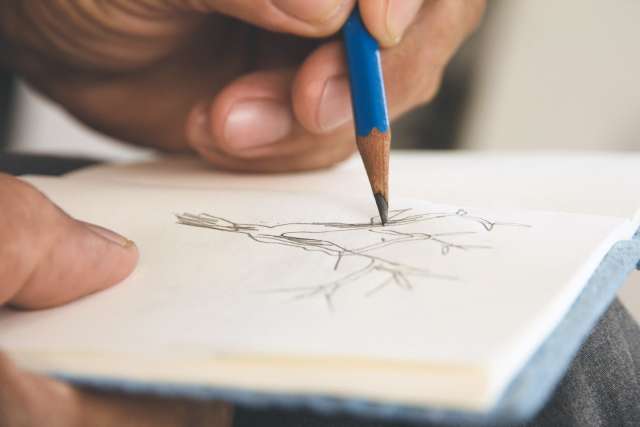 A hand sketches with a pencil on a page in a notebook.