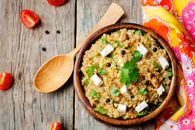Bowl of grain salad with crumbled cheese, herbs and cherry tomatoes