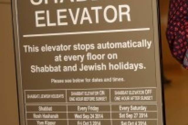 A sign for a "Shabbat Elevator" explaining that the elevator stops automatically at every floor on Shabbat and Jewish holidays, with a partial list of dates and times.