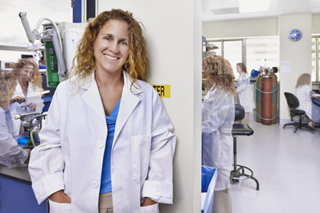 Dr. Joanne Weidhaas leaning on a wall in a laboratory, smiling and looking at the camera.