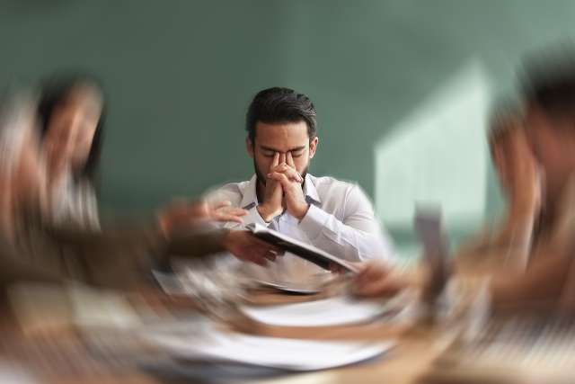 Focused man reading documents at a table while colleagues around him are blurred