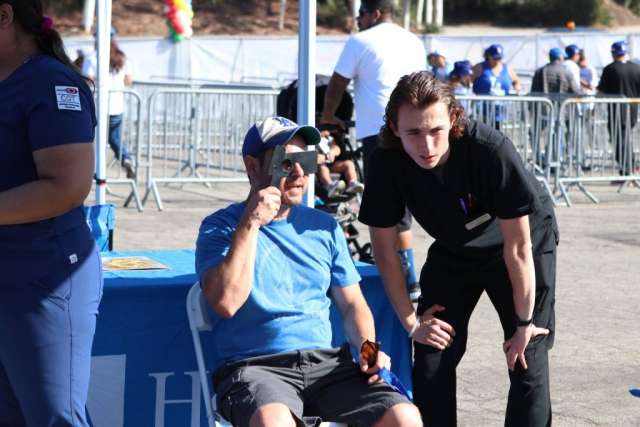 Man in wheelchair waving beside staff at outdoor event booth