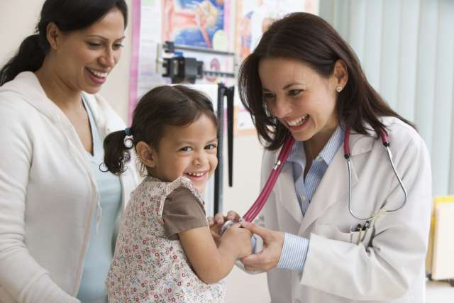 Female doctor placing stethoscope on smiling girl while her mother watches