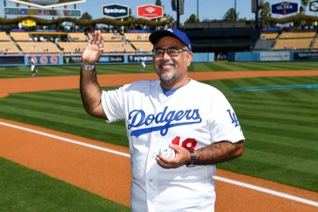 Santiago Munoz III, wearing a Dodgers jersey and cap, stands on a baseball field and waves to the crowd.