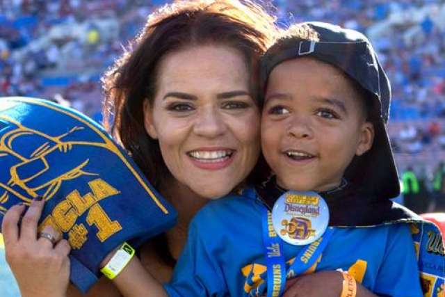 Smiling woman hugs Jackson Verner who is in UCLA gear holding a foam finger at a stadium event.