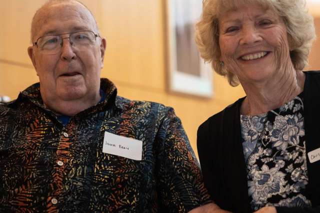 John F. smiling with woman, both seated and holding hands