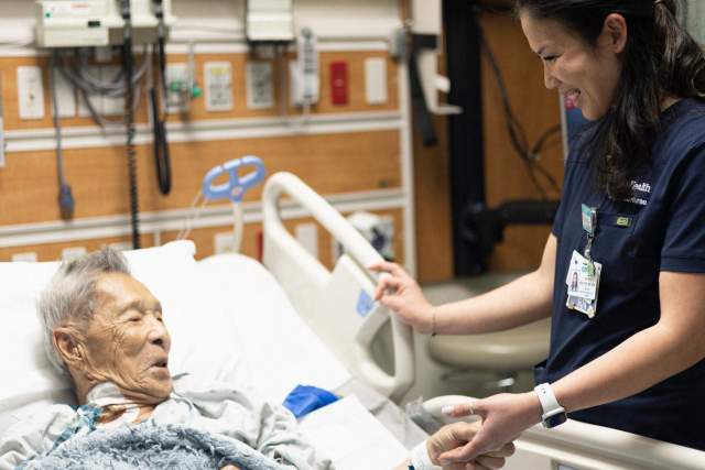 Nurse assisting an elderly patient in a hospital bed.