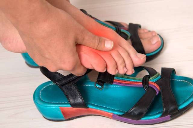 Person pressing red area on foot while wearing a sandal