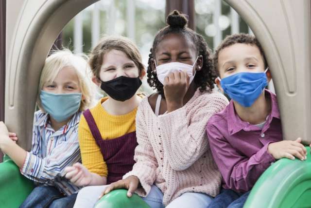 Four children seated together on a playground structure, smiling and interacting.