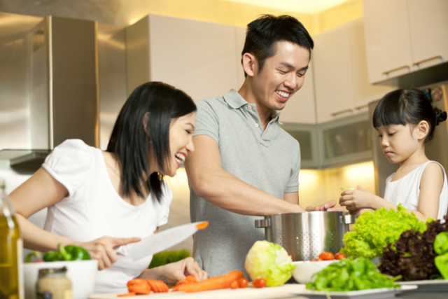 Family preparing a healthy meal together in the kitchen, smiling and chopping vegetables at the counter.
