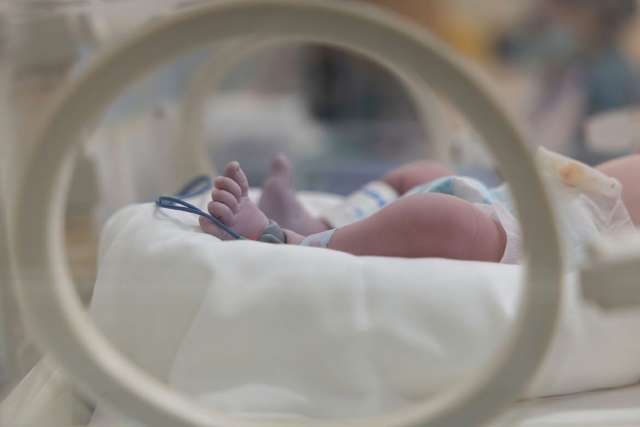 Newborn baby's feet visible through a circular incubator opening.
