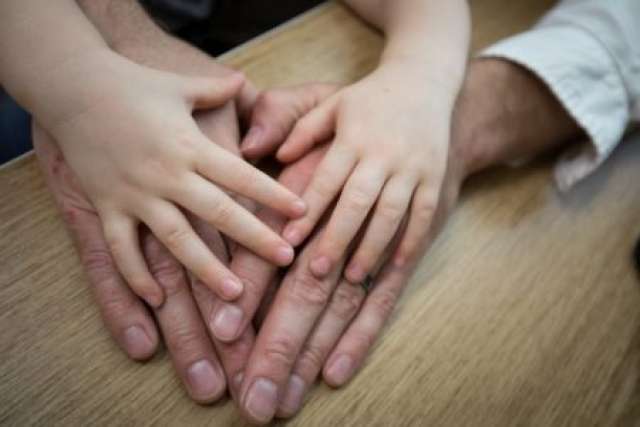 Close-up of two adult hands and two child hands resting together on a wooden surface, showing a gesture of connection and care.