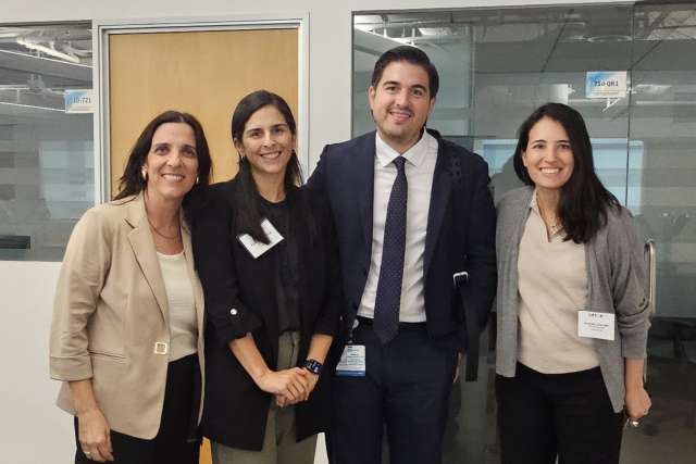 Four professionals in business attire standing and smiling in an office
