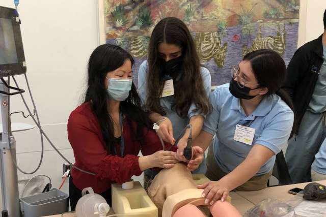 Three allied health students practice medical procedures on a simulation mannequin.