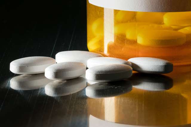 Prescription bottle with blank label for copy space and white pills or tablets on metal table for opioid epidemic illustration.