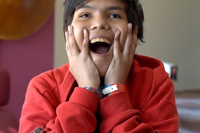 A young boy with a surprised expression on his face, in a red hoodie inside of an office