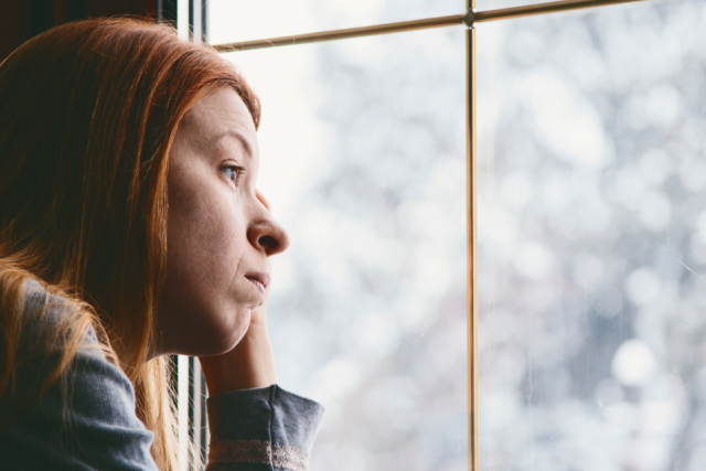 A woman looking out a window at the snow outside.