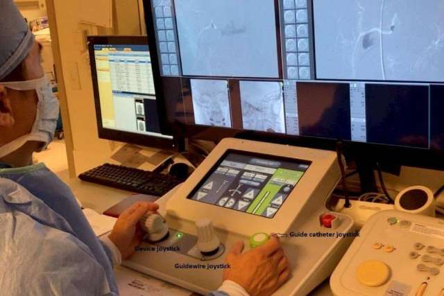 Medical professional operating a robotic system with joysticks and touchscreen while monitoring multiple screens showing imaging scans.