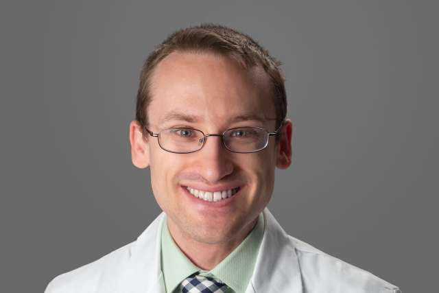 Person in white lab coat and checkered tie with face obscured